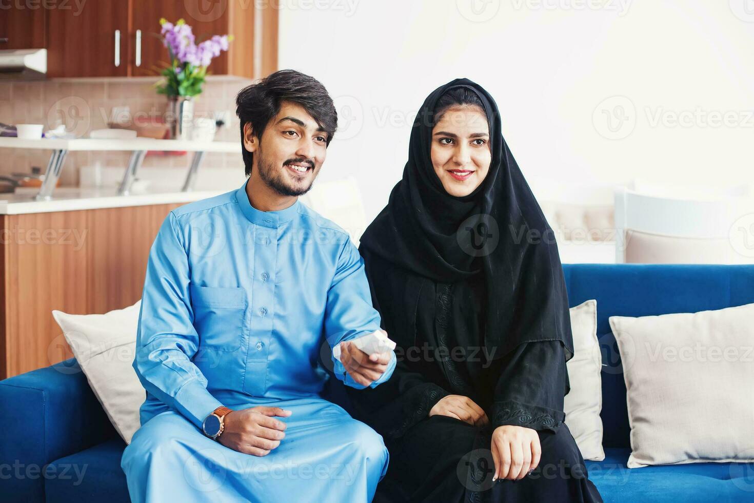 Muslim man and woman using remote control to watch smart tv at home photo