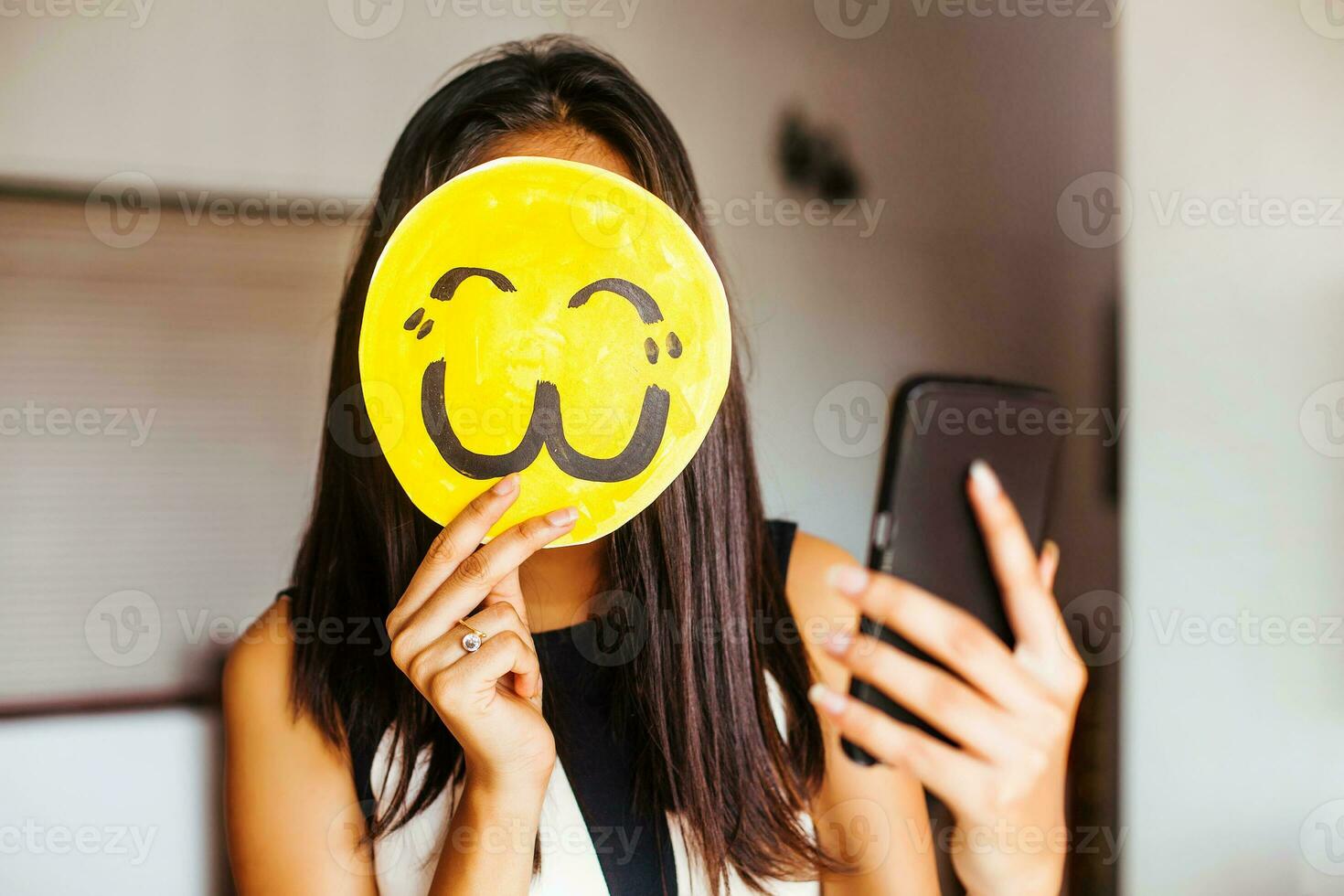 joven indio mujer tomando un selfie con su cara cubierto por un emoji foto