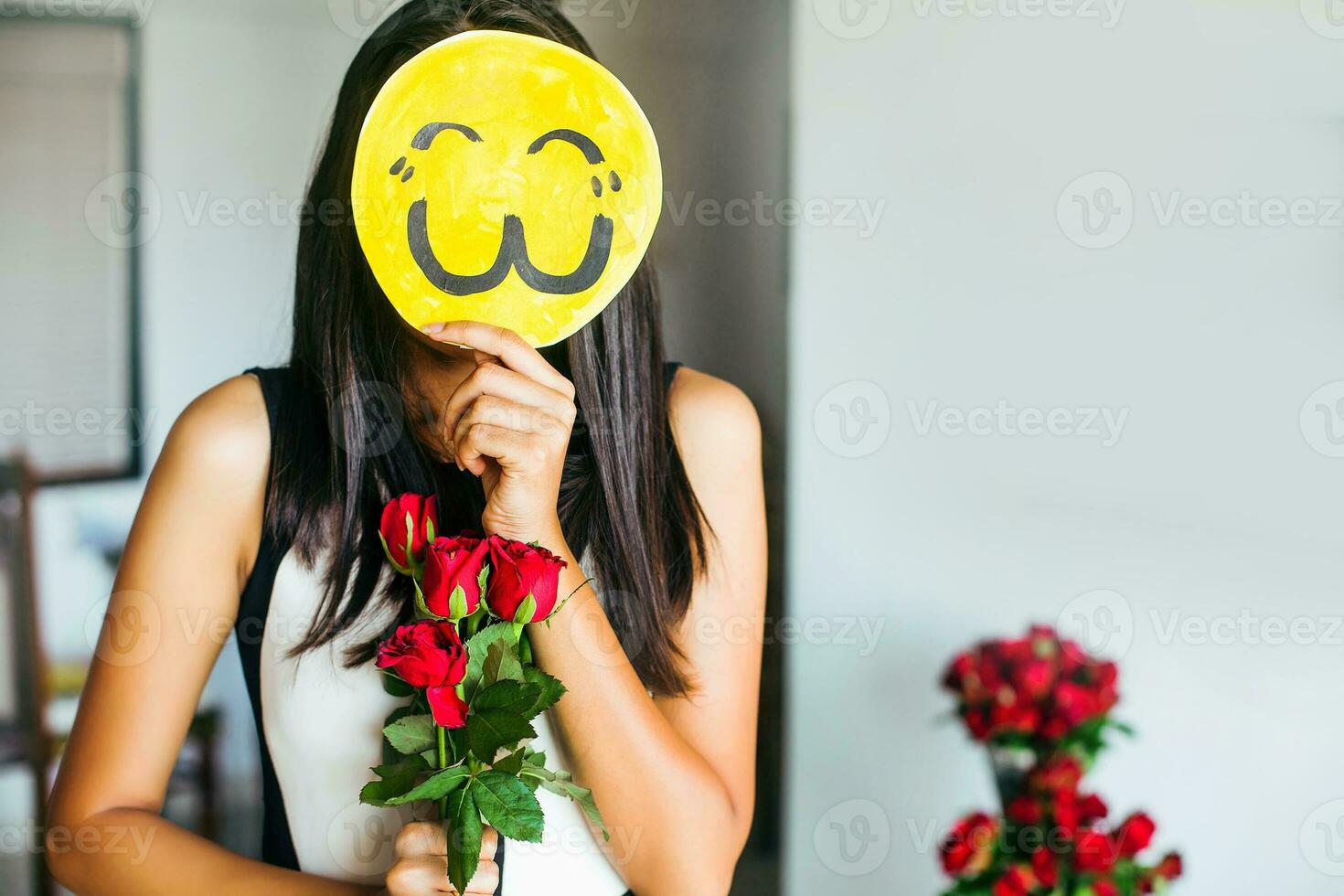 Young indian woman posing with a bunch of roses and her face covered with an emoji photo