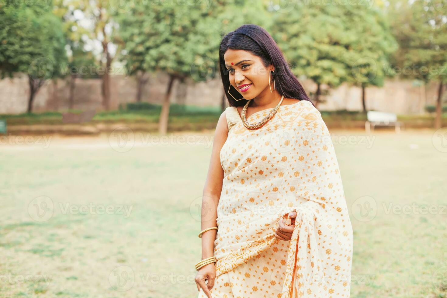 Beautiful Indian young woman in stylish saree walking in the park photo