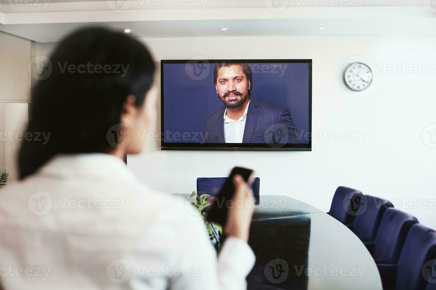 joven indio mujer haciendo vídeo conferencia con director de su empresa en línea en un grande pantalla televisión foto