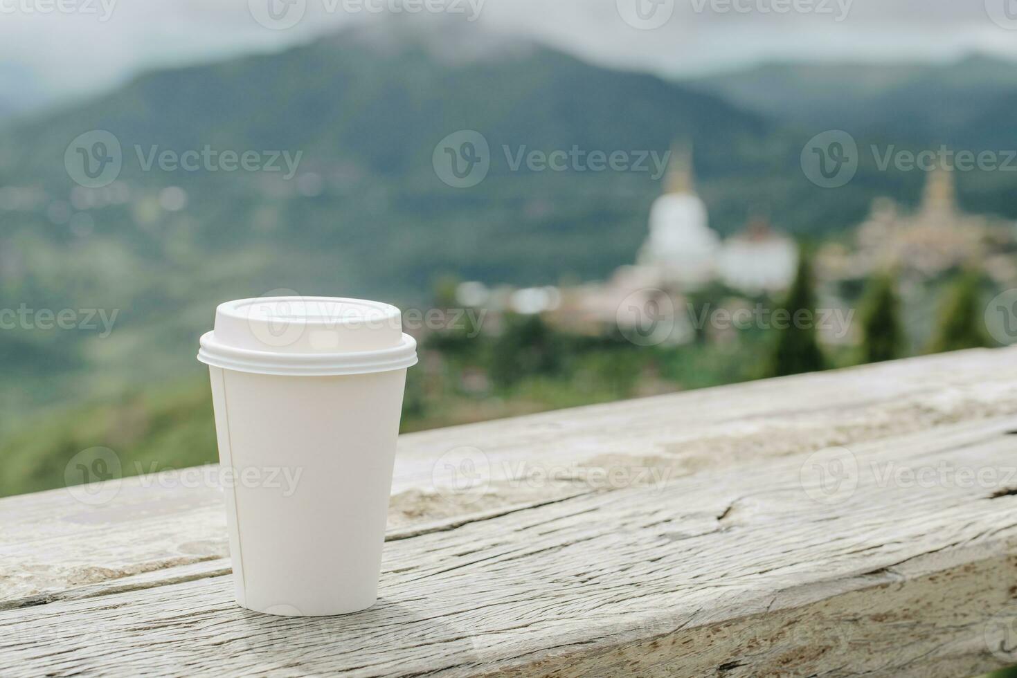 A paper cup of coffee on the wooden table with a spectacular view. photo