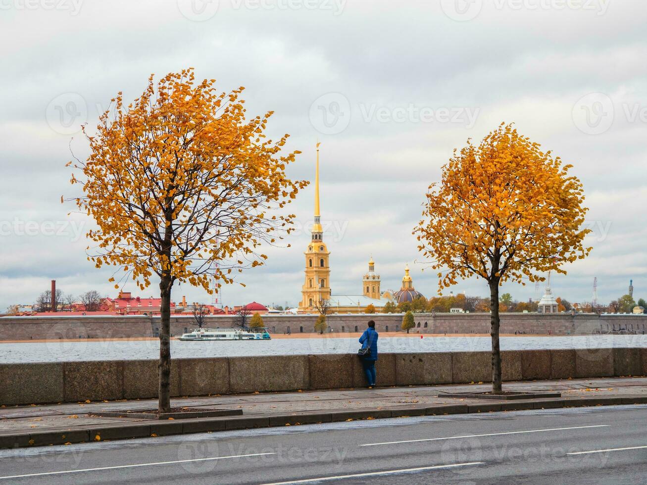 Yellow autumn trees on the granite embankment in St. Petersburg with people walking in autumn. photo