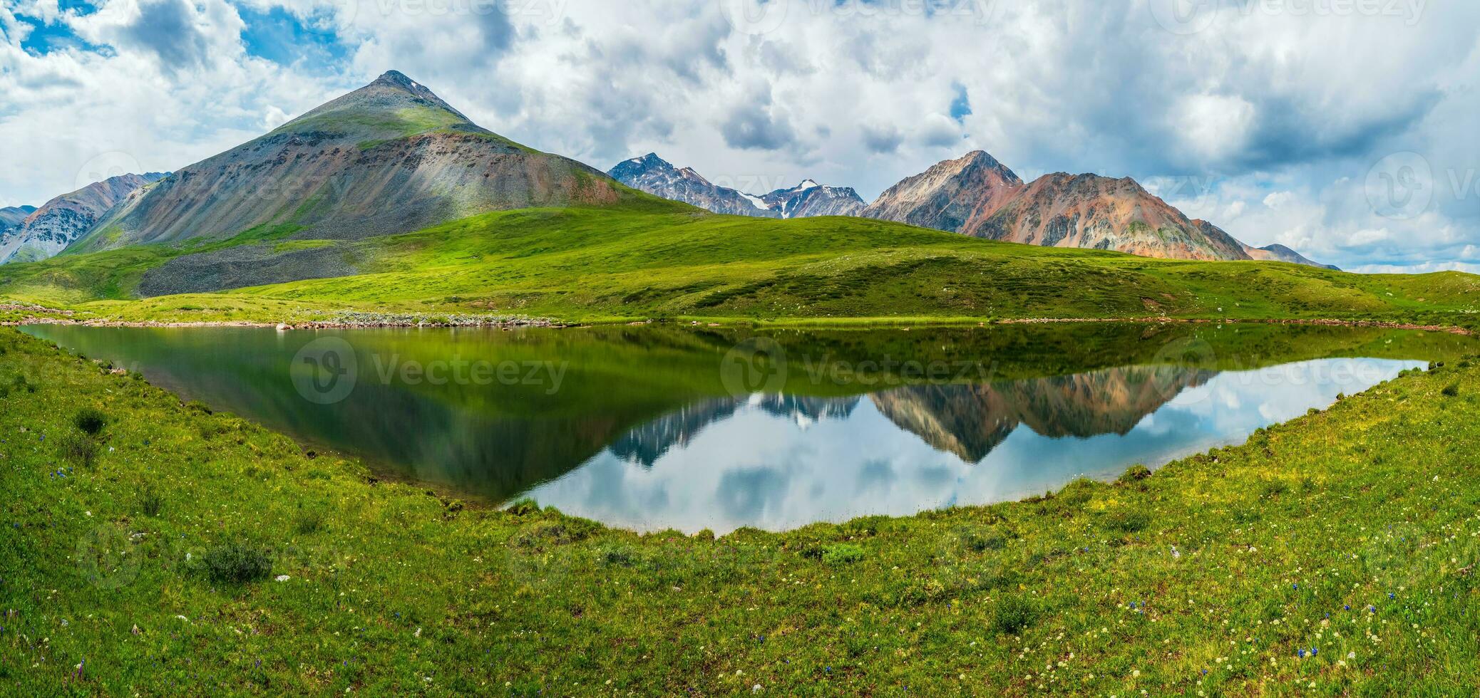 Bright green blue alpine landscape with mountain lake in highland valley in sunlight and big mountain under blue cloudy sky. Shadow of clouds on green mountain valley. Panoramic views. photo