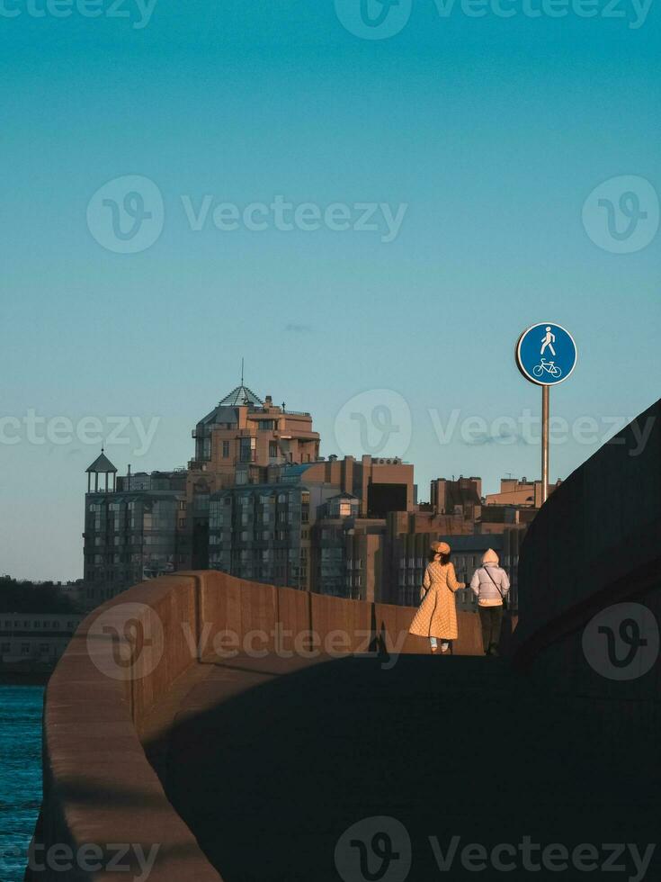 lesbian couple from behind walks across a bridge, with the city landscape in the background photo