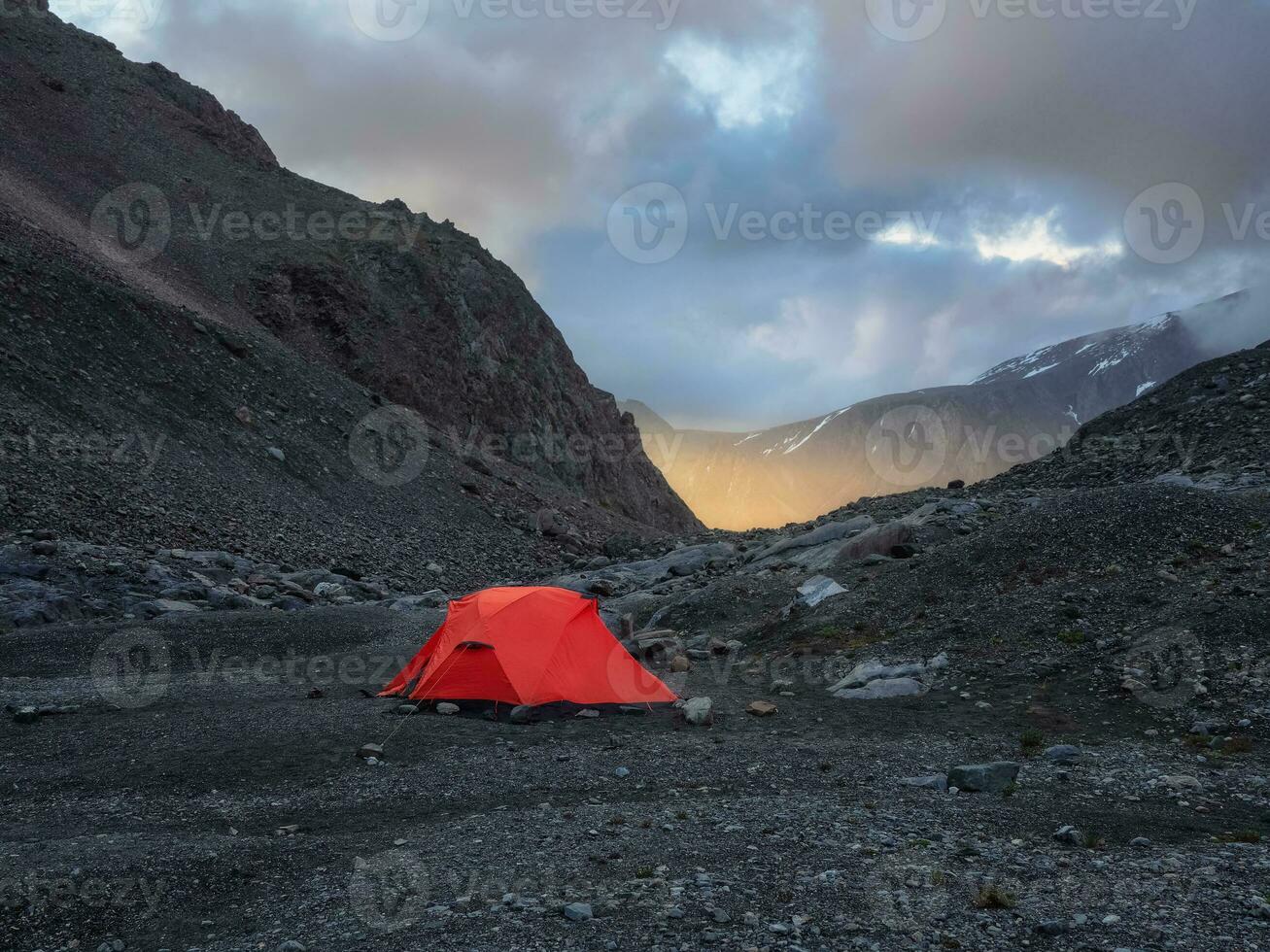 Surrealist alpine landscape with tent on rocky hill among rocks in sunrise. Beautiful morning mountains in low clouds. Surreal scenery with tent in highlands in overcast weather. photo