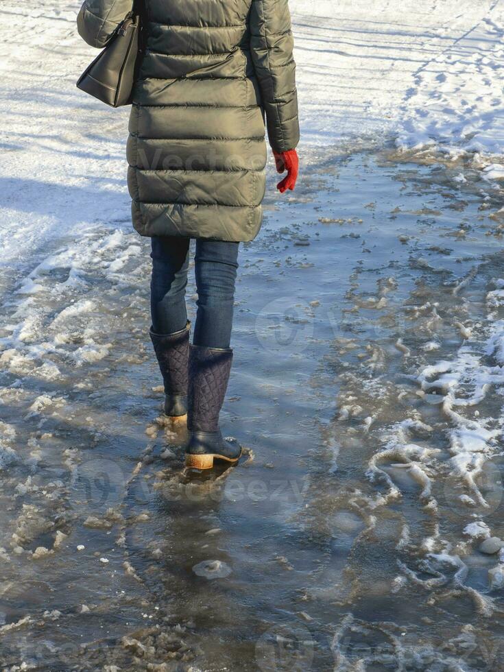 Ice-crusted ground, a woman walking on a slippery street, spring weather. Icy conditions photo