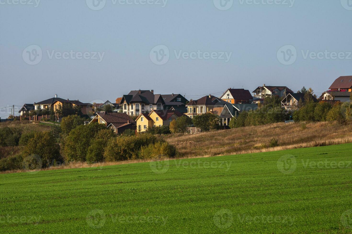 Country life. A village on a hill. A green spring field in front of a modern village on a hill against a clear blue sky. photo