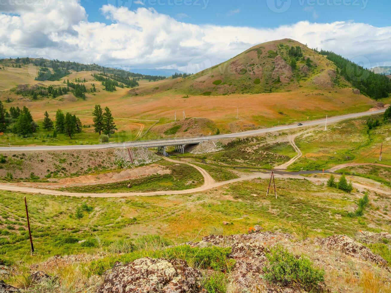 Picturesque summer mountain landscape with small bridge on the road through the pass. Turn on the asphalt mountain highway. Chuysky tract and a view of the North Chuysky Mountain range in the Altai. photo