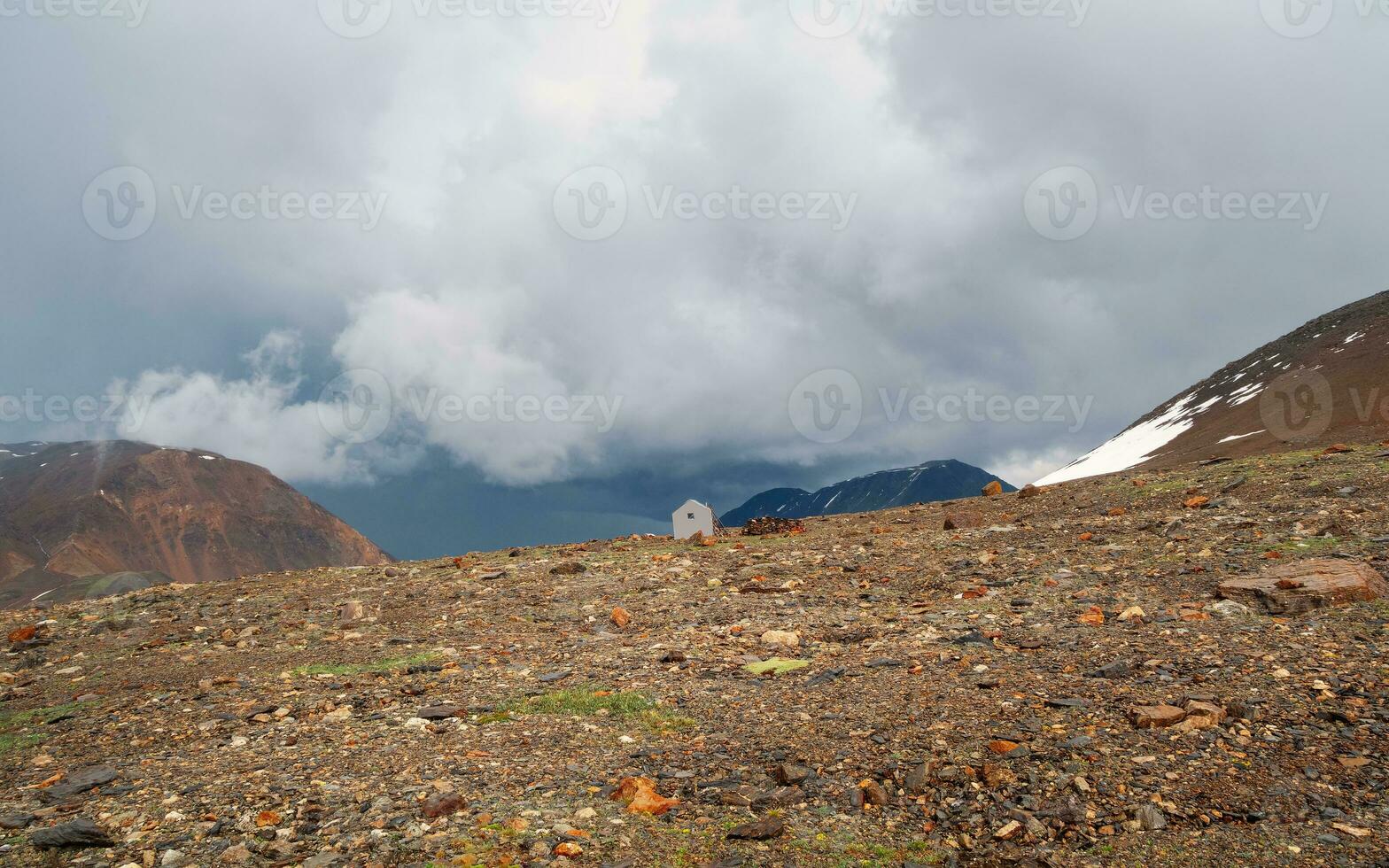 panorámico ver con pequeño antiguo alpinismo casa en el montañas debajo un Tormentoso cielo. vacío alpinismo acampar. auténtico montaña dramático paisaje en el altai montañas. foto