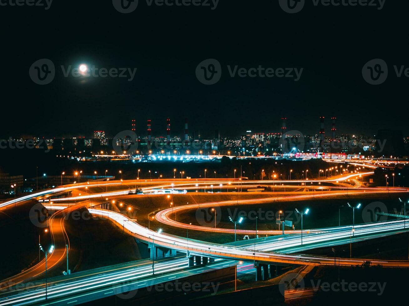 A night road junction in an industrial area of a modern metropolis. Aerial view. Long shutter speed with blurred lights from the headlights photo