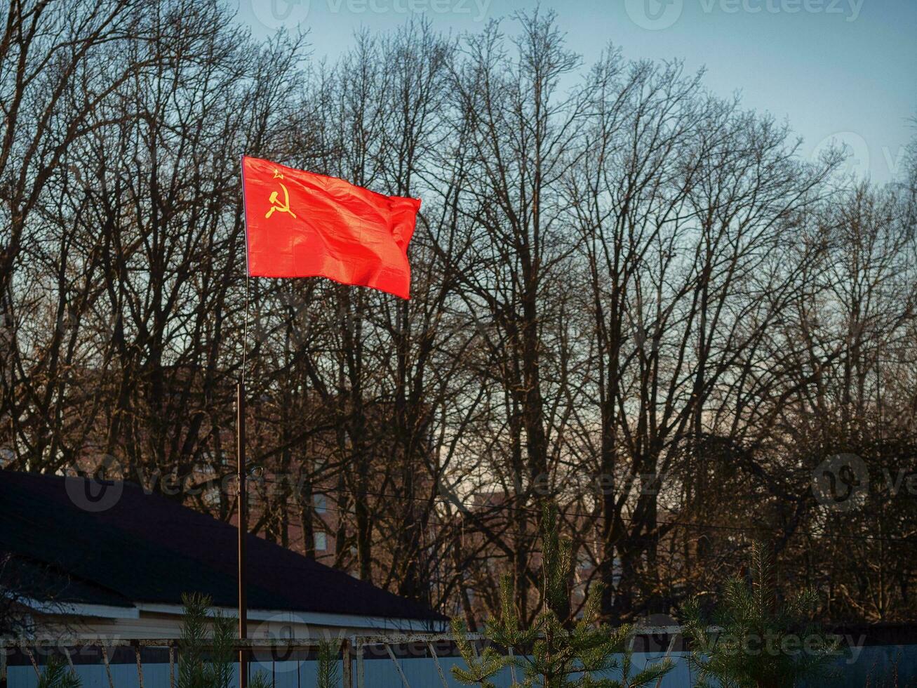 The red Soviet flag glows brightly in the sun on the suburban area behind the fence photo