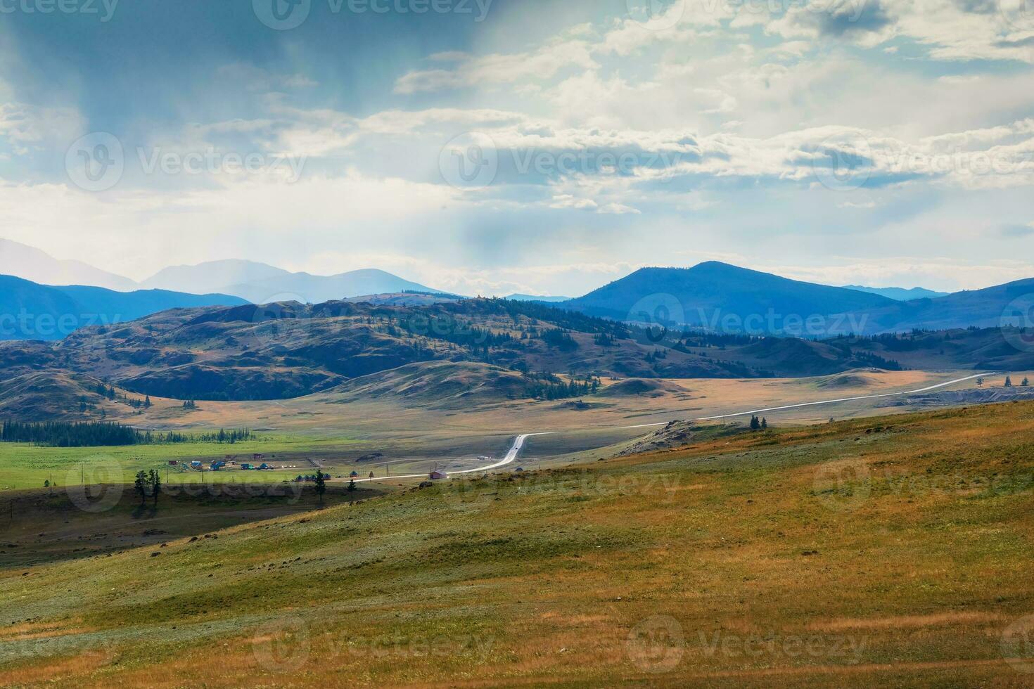 Rainy alpine view from green hills to high snow mountain range in sunlight during dramatic in changeable weather. Winding asphalt road among the hills. photo