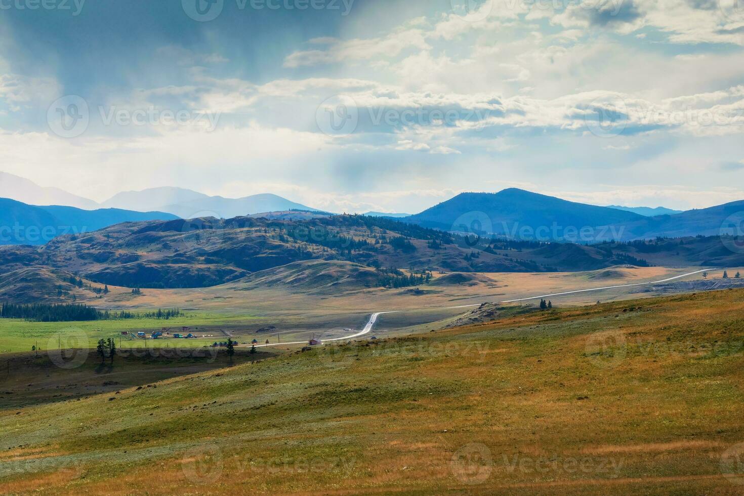 lluvioso alpino ver desde verde colinas a alto nieve montaña rango en luz de sol durante dramático en cambiable clima. devanado asfalto la carretera entre el sierras. foto