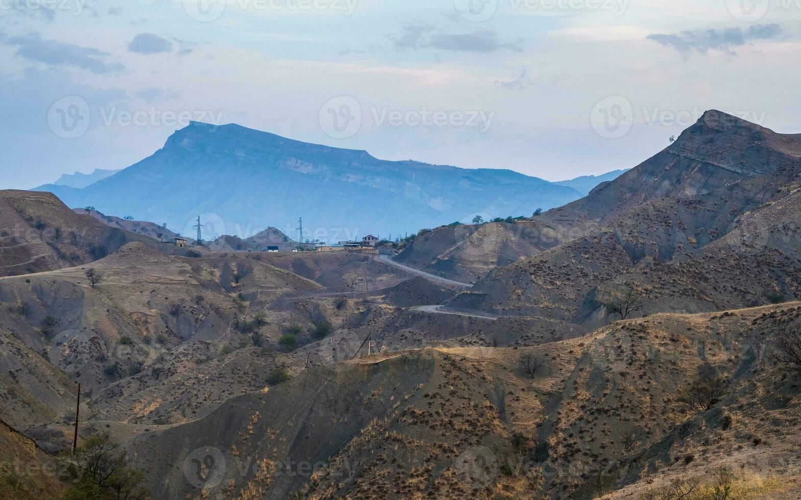 Panorama of the evening mountains with a complex landscape. Mountain serpentine in the dawn sunlight. Dangerous narrow dirt mountain road through the hills to a high-altitude village. photo