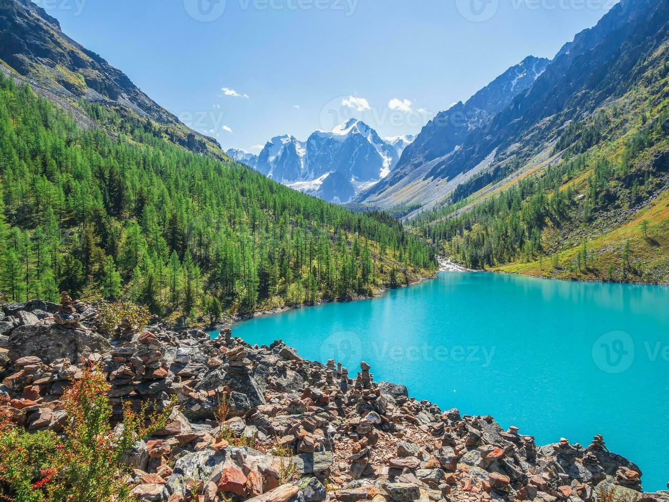 Amazing clear mountain lake in forest among fir trees in sunshine. Bright scenery with beautiful turquoise lake against the background of snow-capped mountains. Lower Shavlin Lake photo