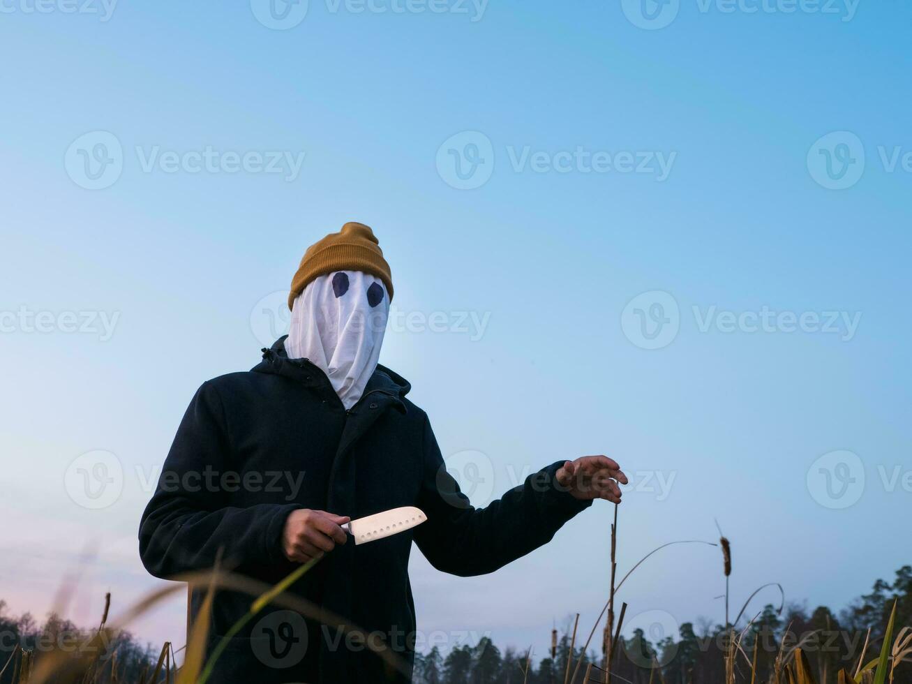 Dangerous man with a white cloth on his face and a knife in his hand on the street in the evening. Halloween. photo