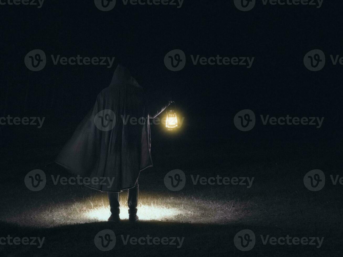 Man in motion in black clothes holding the glowing lantern on the dark background photo