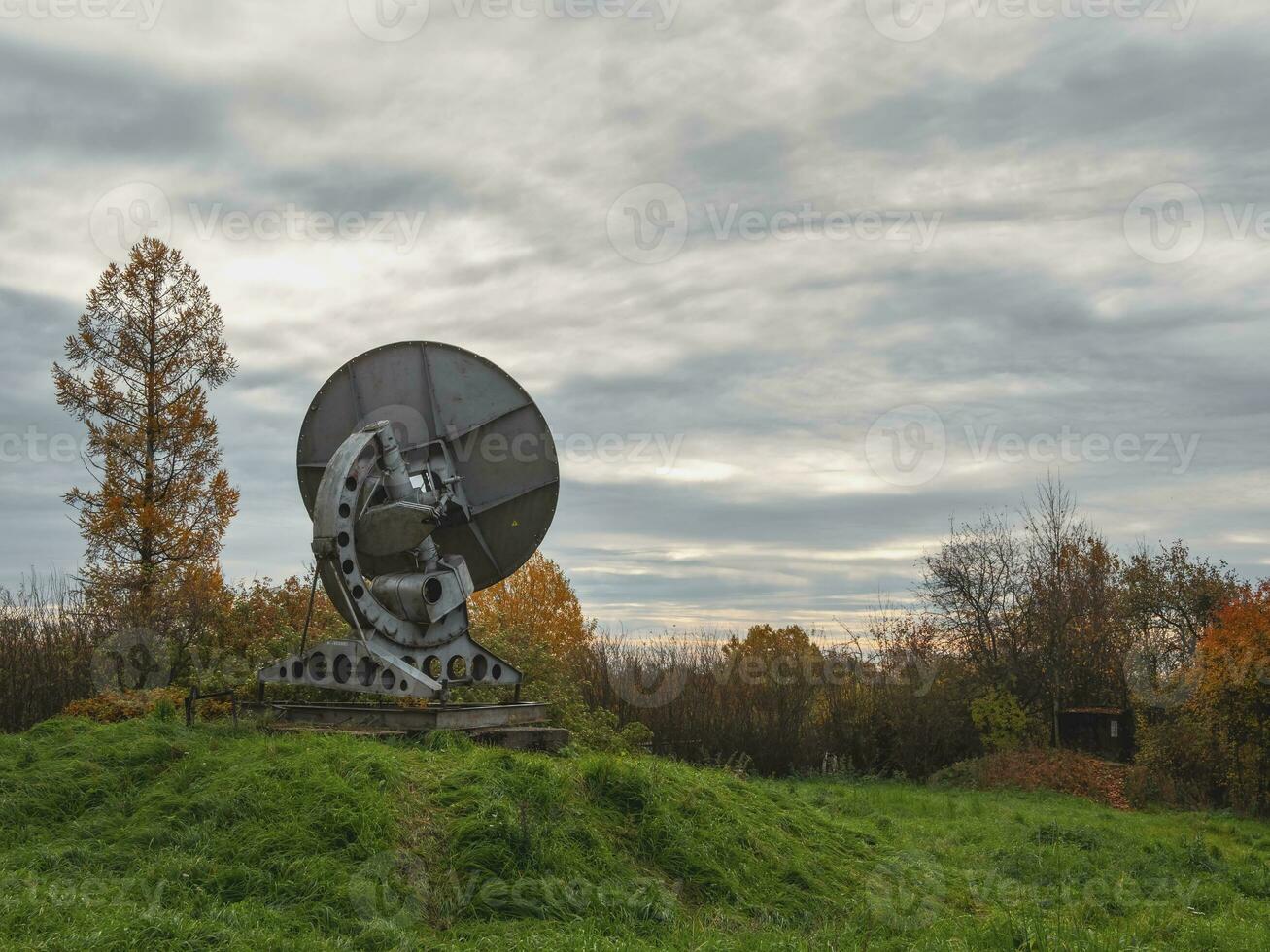 Vintage telescope a large satellite dish on a background of observation forest and cloudy sky, radar in the past. Technology concept, search for extraterrestrial life, wiretap of space. photo