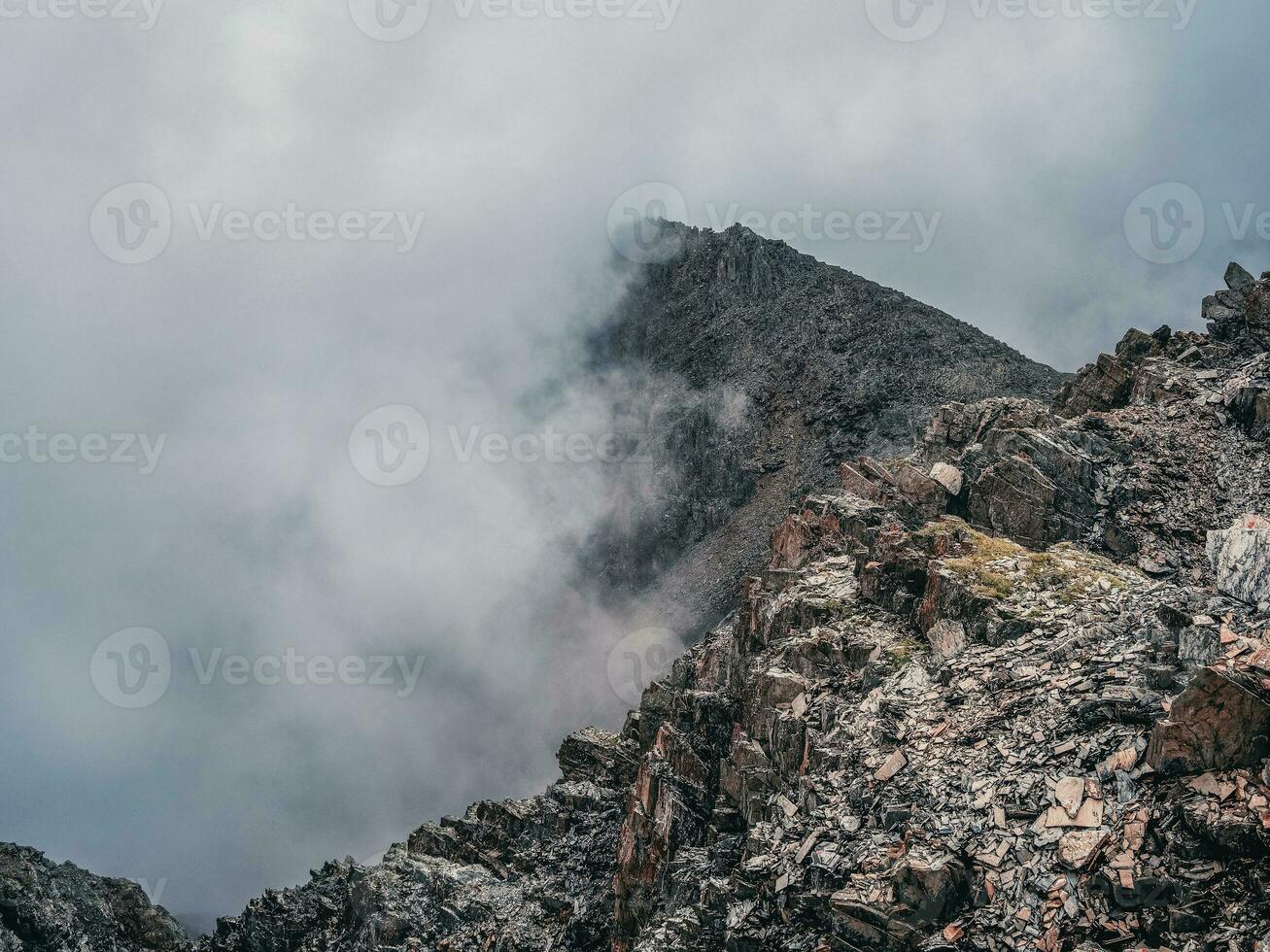 Mountain view from cliff at high altitude. Mystical landscape with beautiful sharp rocks near precipice and couloirs in low clouds. Beautiful mountain foggy scenery on abyss edge with sharp stones. photo