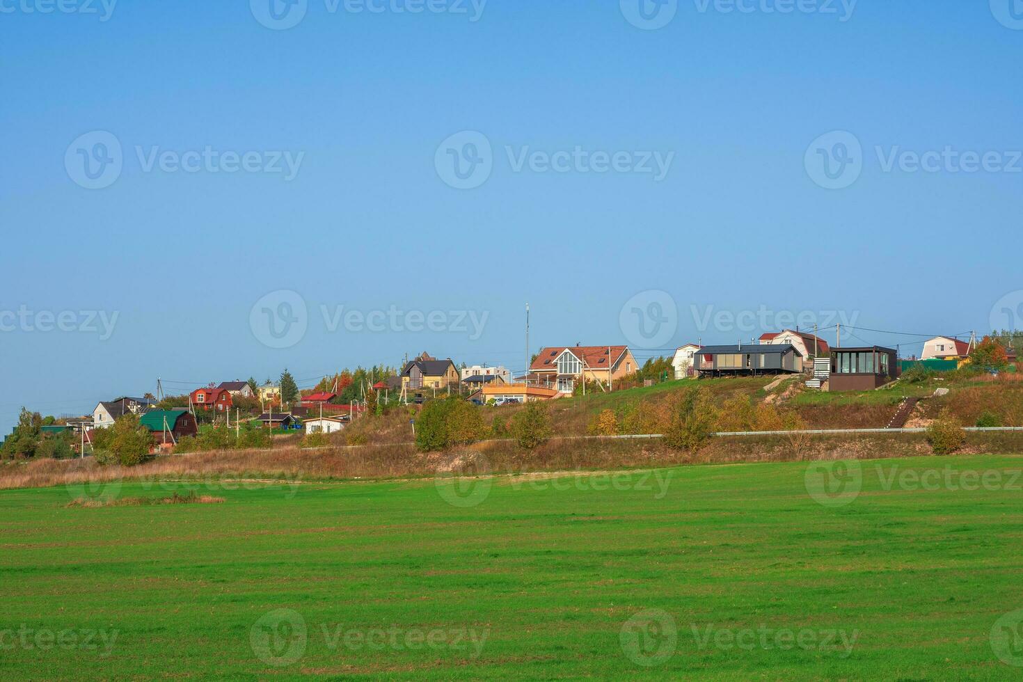 Country life. A green spring field in front of a modern village on a hill against a clear blue sky. Agricultural land. photo