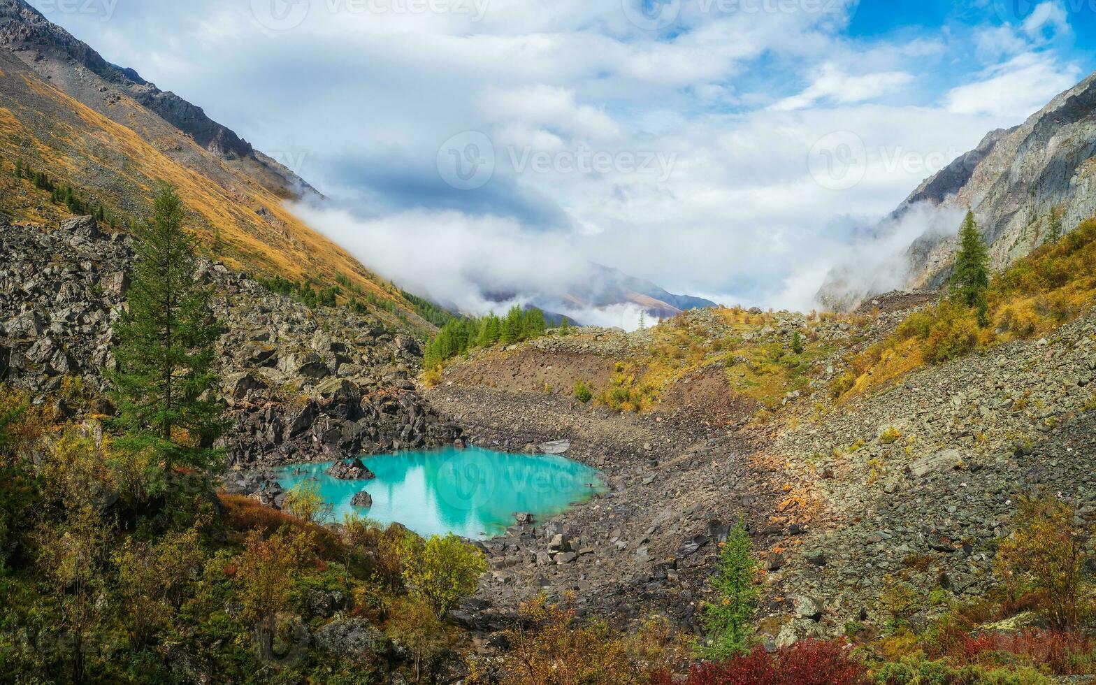 Panoramic view of the autumn mountain, fog over the mountain slopes in the distance, white clouds filling the mountain gorge. A clear blue mountain lake and a bright autumn forest. photo