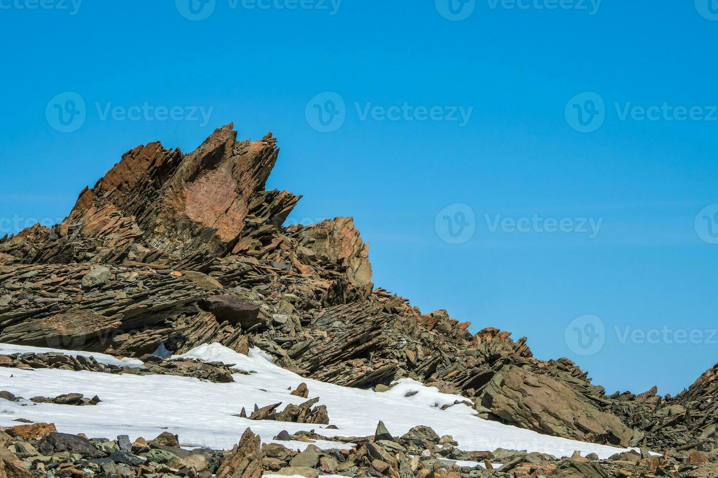 Sharp rocks. Highland scenery with sharpened stones of unusual shape. Awesome scenic mountain landscape with big cracked pointed stones closeup among snow under blue sky in sunlight photo