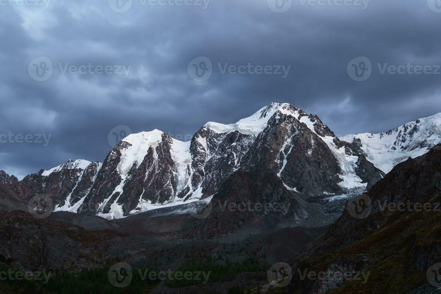 oscuro atmosférico alpino paisaje con cubierto de nieve montaña parte superior debajo noche cielo. increíble paisaje con hermosa puntiagudo pico con nieve y alto Nevado montaña pared con oscuro bajo nubes foto