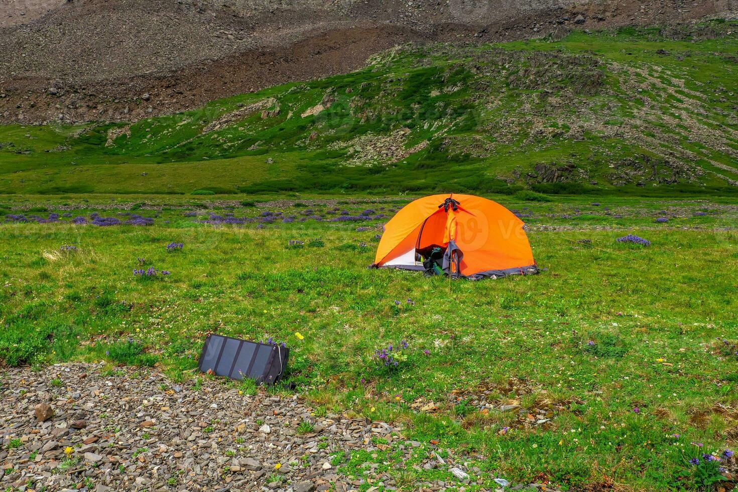 Solar battery at the campsite. Solo hiking in the picturesque summer mountains. Camping on a summer green rocky high-altitude plateau. photo