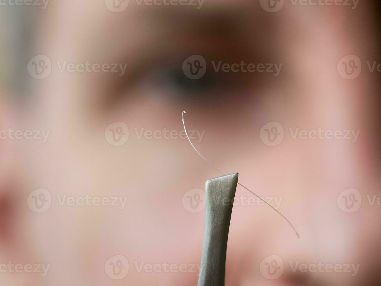 Tweezers with gray hair in front of the woman face. photo