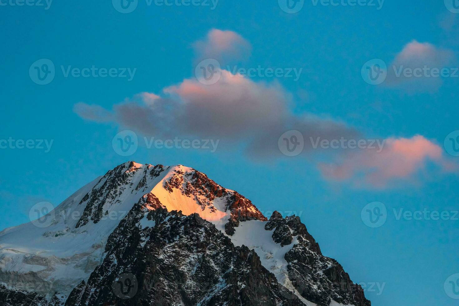 Top black rocks in evening golden sunshine and white-snow pointy peak. Atmospheric dawn landscape with high snowy mountain with peaked top. photo