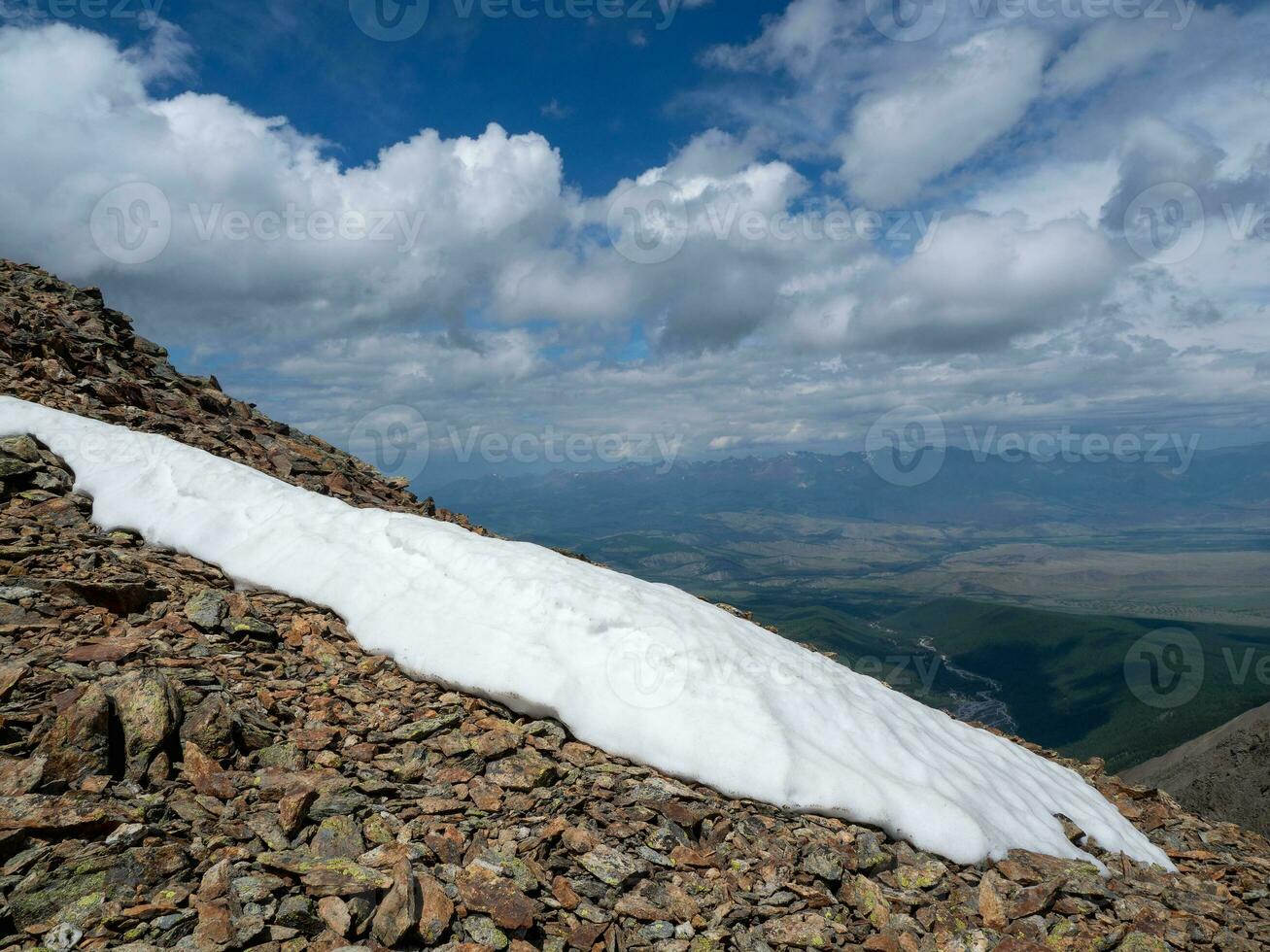 Snowfields on a mountain slope. Dangerous cliff. Atmospheric scenery on top of mountain ridge. Snowy high-altitude plateau. Scenic view from precipice edge under blue sky to snowy mountains. photo