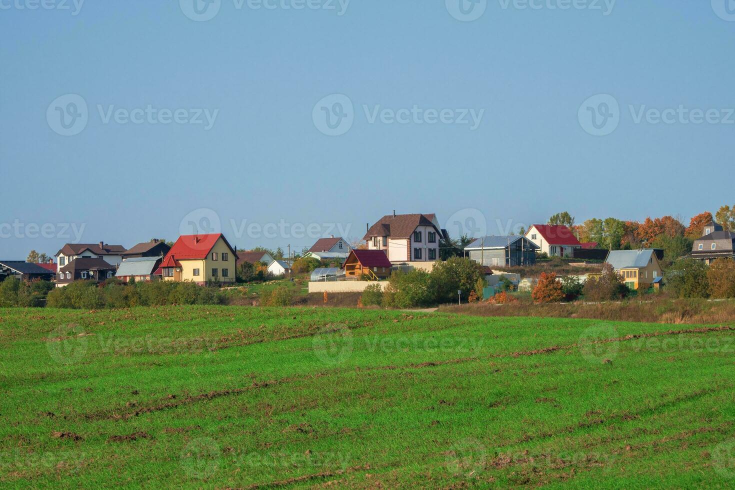 un verde primavera campo en frente de un moderno pueblo en un colina en contra un claro azul cielo. agrícola tierra foto