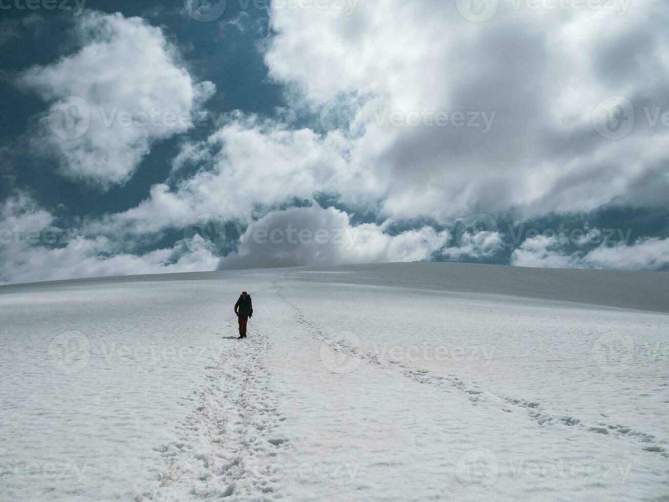 Solo hiker on the glacier. Extreme recreation and mountain tourism. A male hikers go up the mountain path. In the background, blue cloudy sky. photo