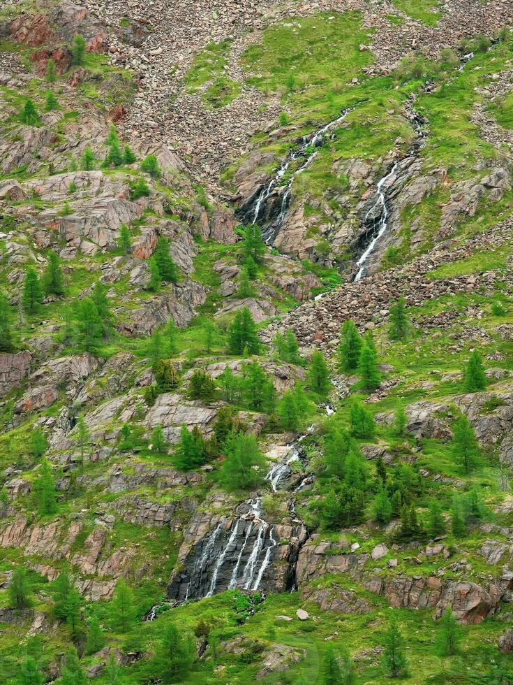 Waterfall sleeves. Scenic distance alpine landscape with trees in slope green rocky big mountain range with waterfall  in sunny light. Colorful natural landscape with a waterfall on a sheer cliff. photo