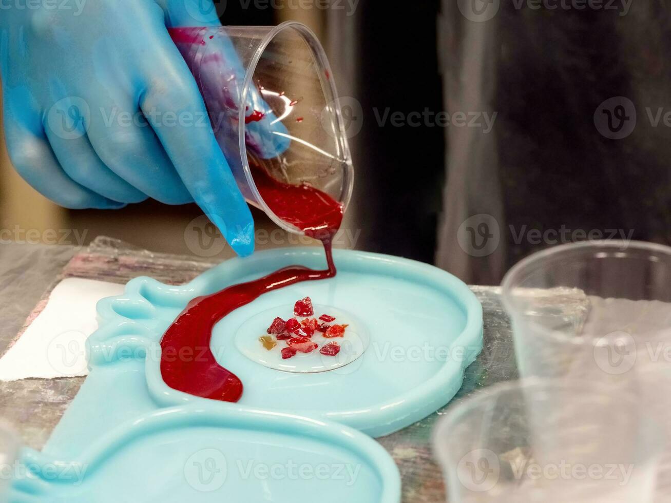 The art process of pouring epoxy resin into a wooden toy. Technology process of creating a painting in style resin art, works with epoxy in studio, makes a wooden stand with the image. Close up. photo