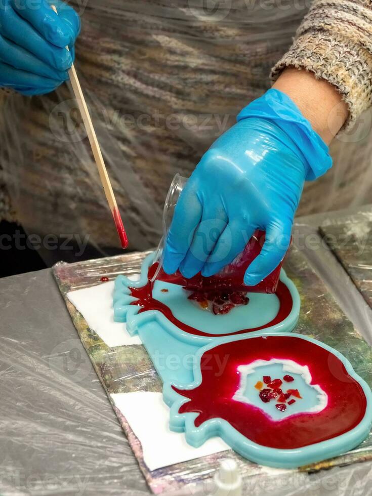 The art process of pouring epoxy resin into a wooden toy. Technology process of creating a painting in style resin art, works with epoxy in studio, makes a wooden stand with the image. Close up. photo