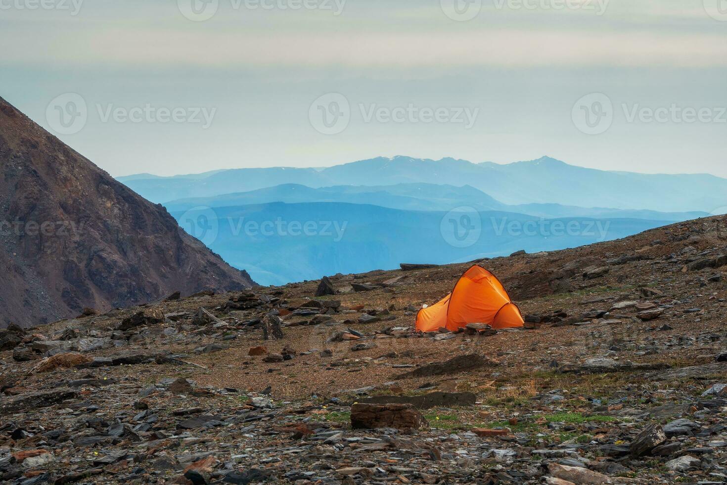 Alpine landscape with tent on rocky hill among rocks in sunrise. Surreal scenery with tent in highlands in overcast weather. photo