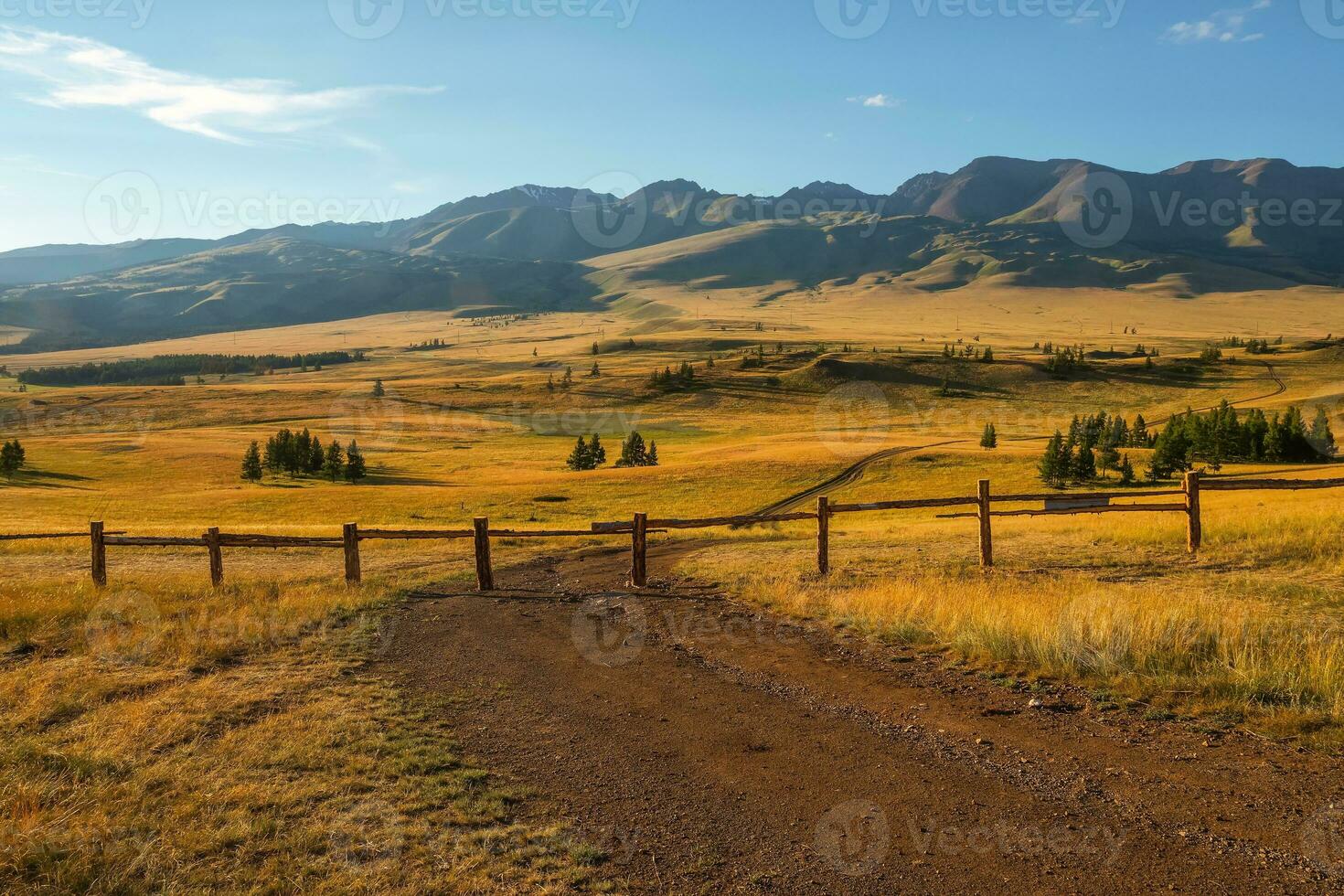 suciedad la carretera es obstruido por un cerca. el camino es cerrado, privado territorio. hermosa soleado paisaje con dorado vasto campo con largo cerca. vívido paisaje con otoño campo detrás madera cerca en montañas foto