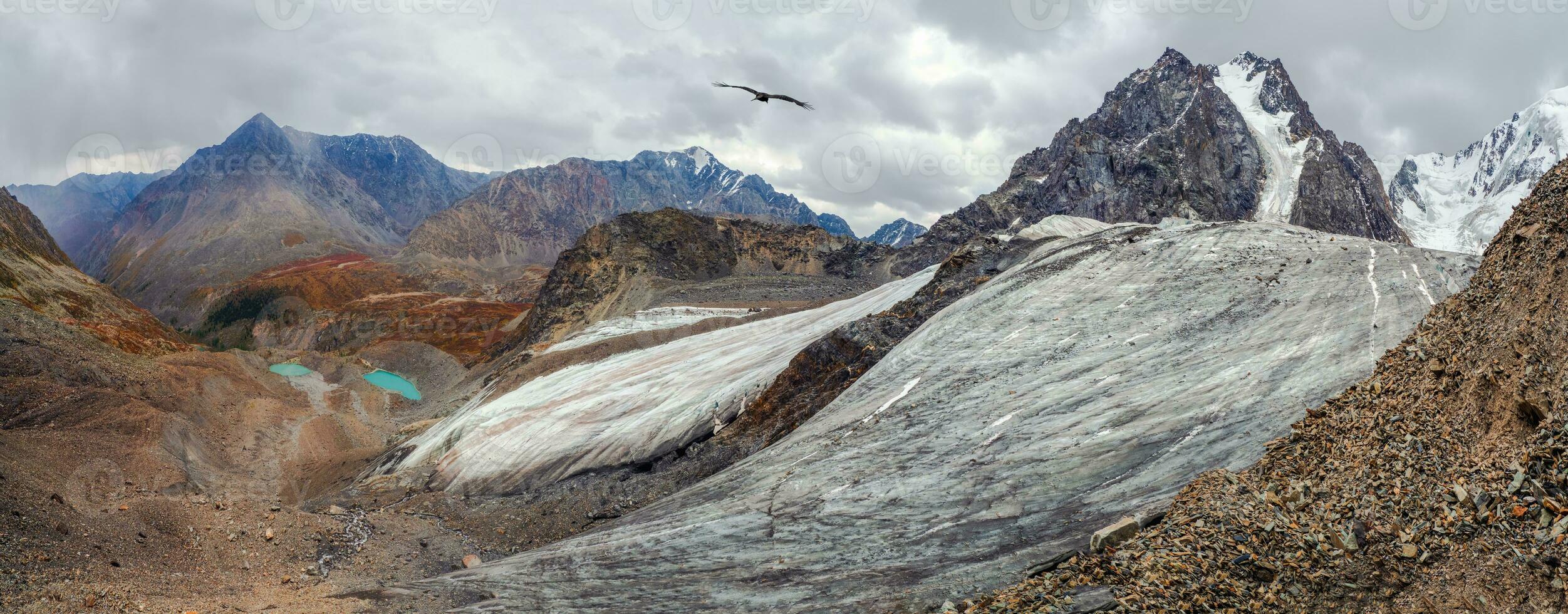 Wide panoramic view of the mountain valley. Mountain landscape with a huge snowy mountain and a glacier illuminated by the sun among high rocks. Stunning alpine scenery with a large glacier and lakes photo