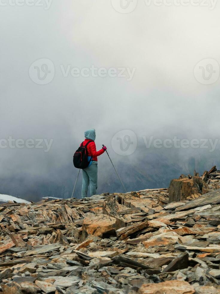 Hard hiking trail. Foggy day in the mountains. Activities woman climb to the top of a misty stone hill. Solo climbing and adrenaline. Extreme sport. People in difficult conditions. Vertical view. photo