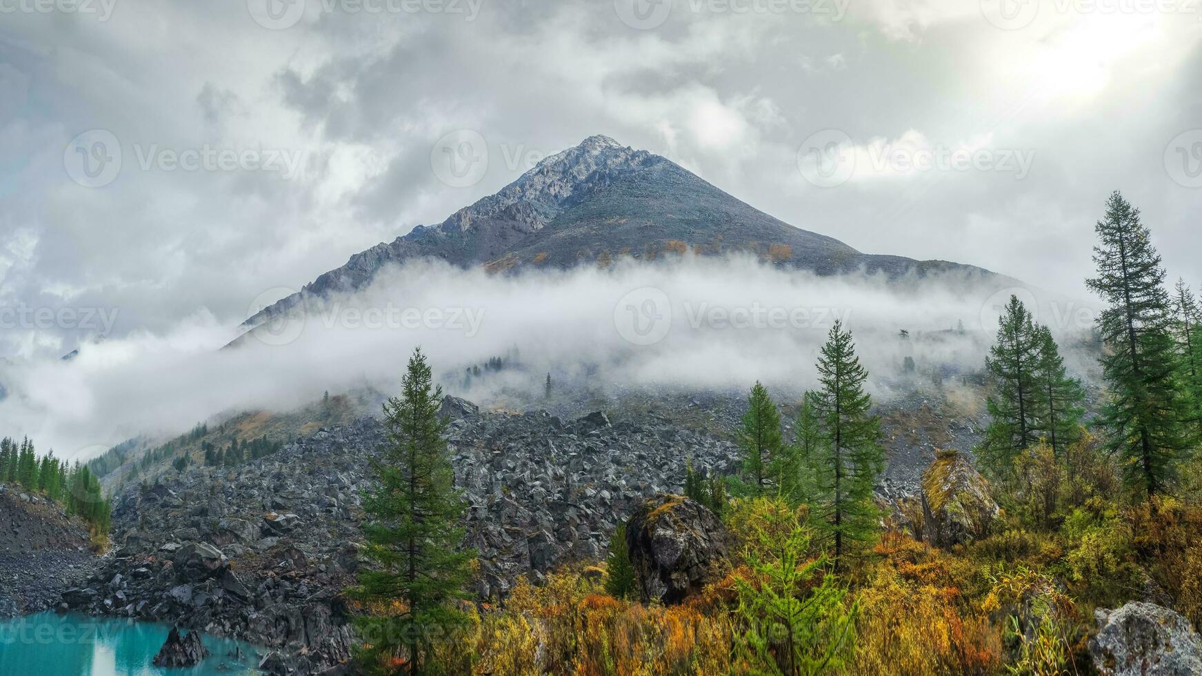Panoramic view of the autumn mountain, a narrow strip of fog over the mountain slopes in the distance, white clouds filling the mountain gorge. A clear blue mountain lake and a bright autumn forest. photo