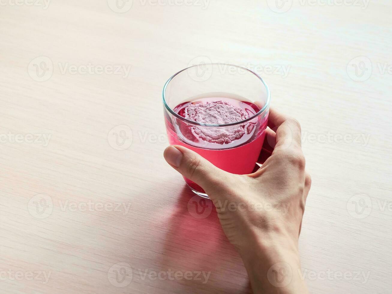 Glass with a fruit drink in hand. Natural berry collagen protein powder in glass of water for skin regeneration. Food additives.  Disposable collagen powder. Copy space. photo