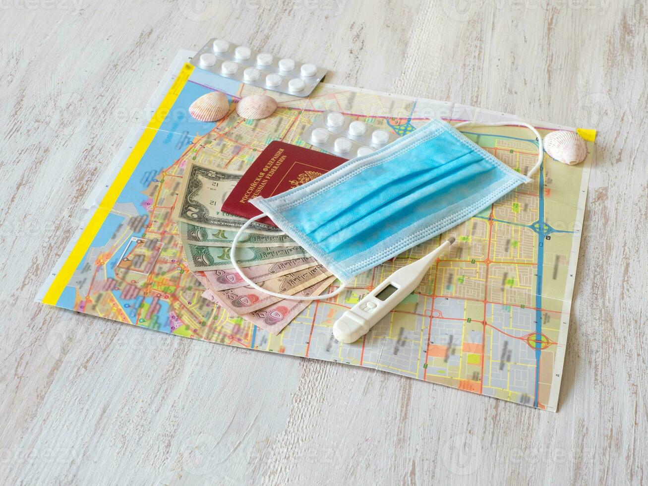 A medical mask, map, pills, passport, and money are laid out on the table. Travel concept photo