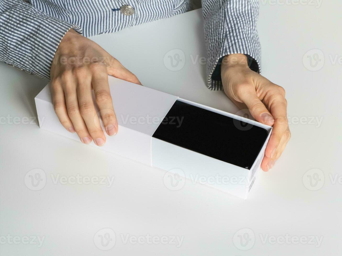 Unpacking a new smartphone on a white table. Female hands holding modern smartphone with blank screen. Online shopping concept photo