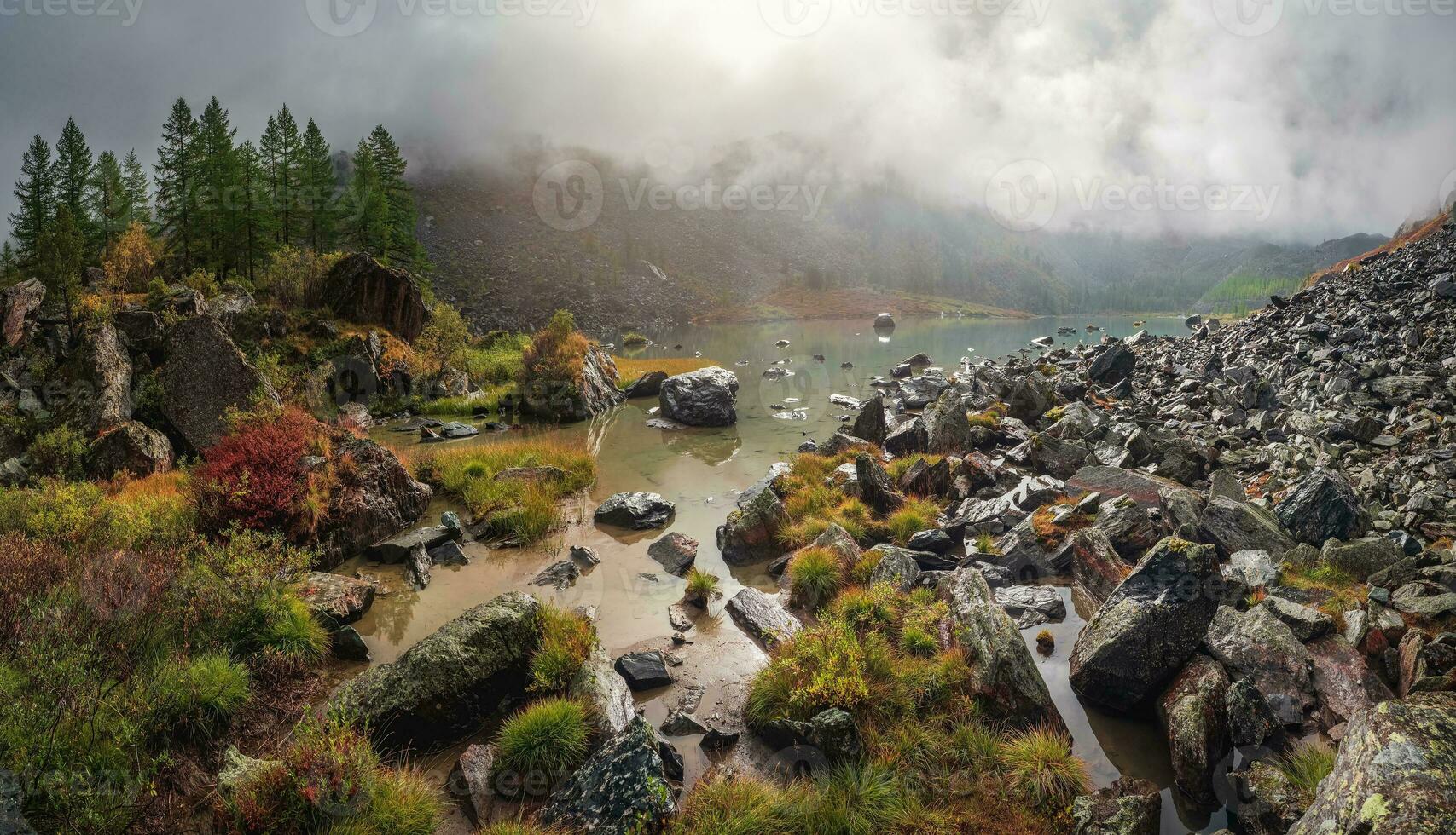 Panoramic view of the autumn mountain, fog over the mountain slopes in the distance, white clouds filling the mountain gorge. A clear blue mountain lake and a bright autumn forest. photo