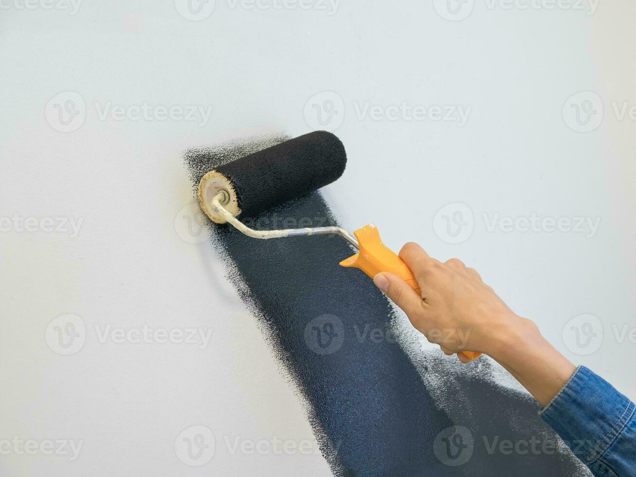 Woman with a roller paints the wall black. Home repair concept. Copy space. photo