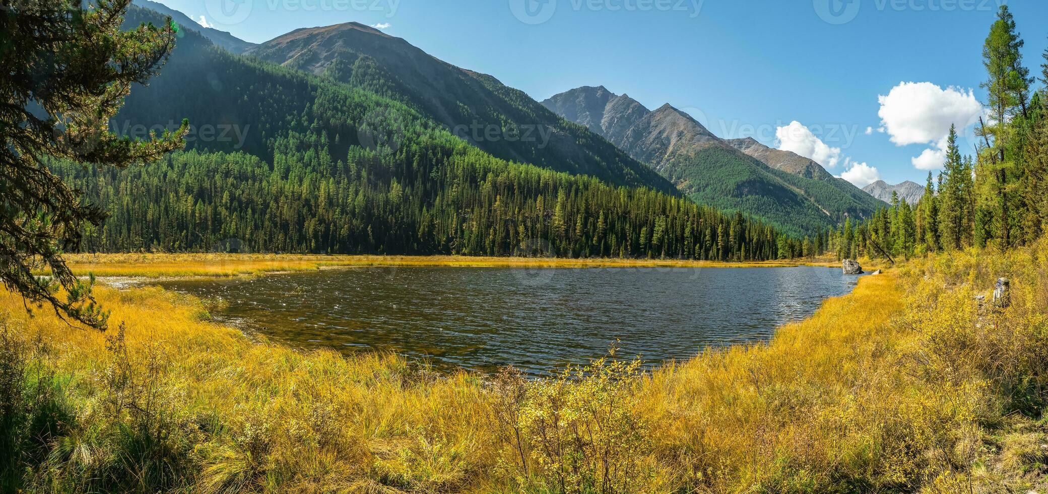 Panoramic view of sunny swampy autumn plateau. Awesome highland scenery with beautiful glacial lake among sunlit hills and rocks against mountain range. photo