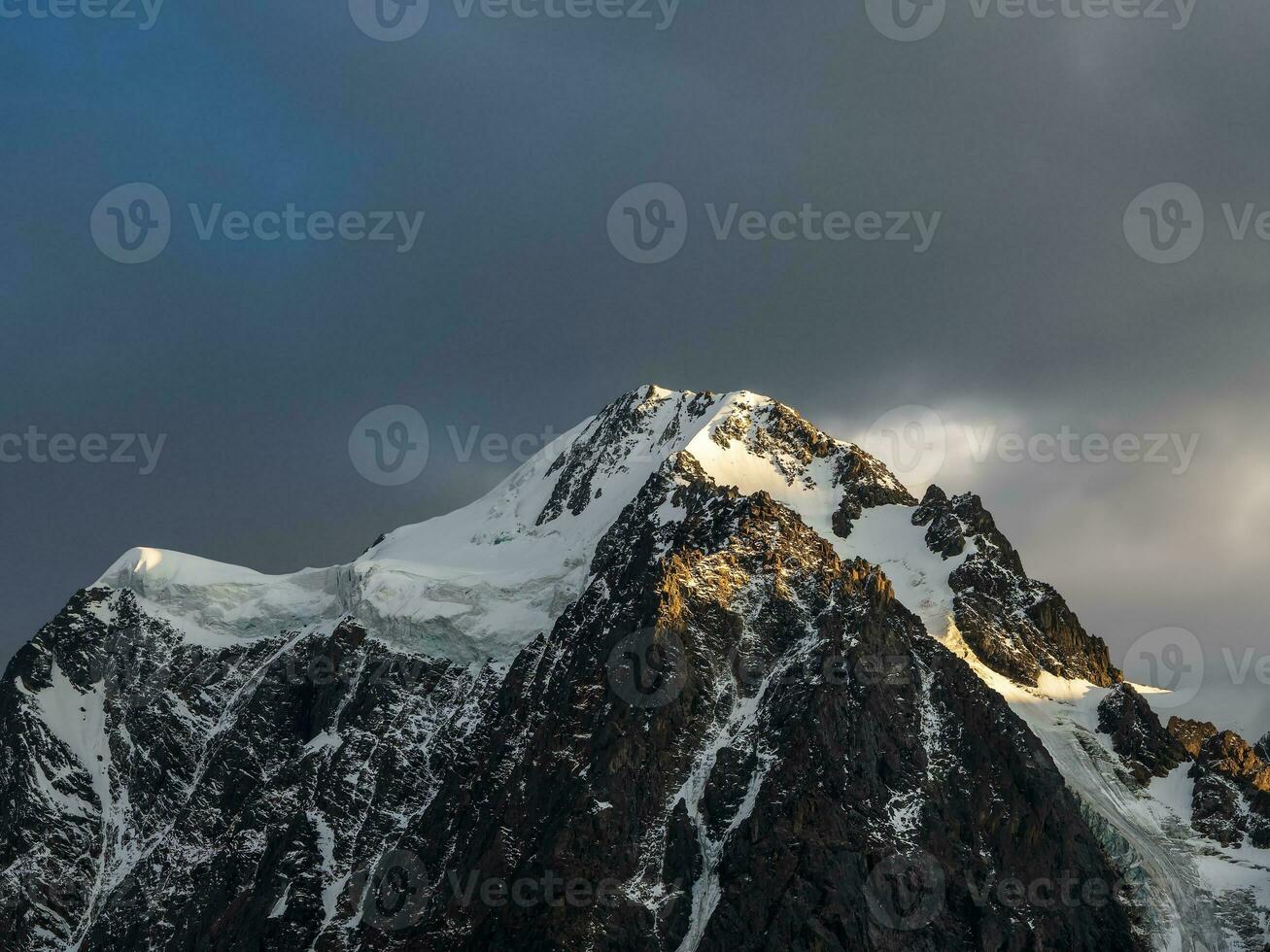 Atmospheric alpine landscape with snow-covered mountain top under evening sky. Awesome scenery with beautiful pointy peak with snow and high snowy mountain wall with low clouds. photo