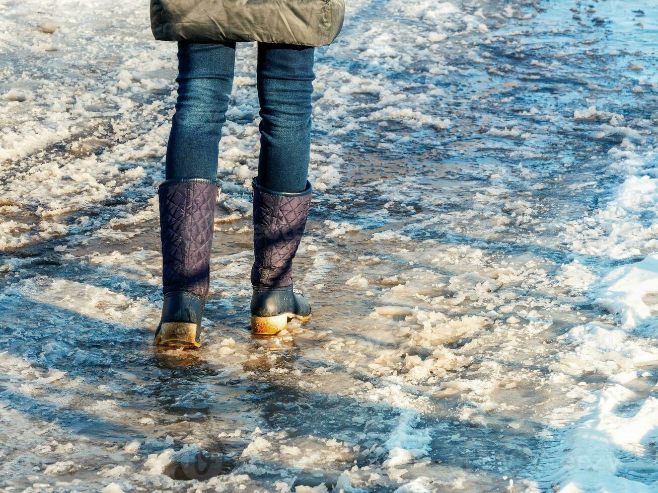 Ice-crusted ground, a woman walking on a slippery street, spring weather. photo